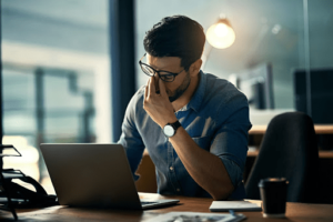 Man rubbing his head while working on his laptop 